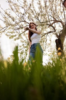 cute woman in light clothes posing next to a flowering tree in the countryside. High quality photo