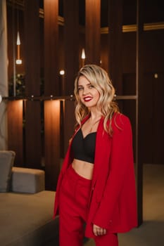 a beautiful girl dressed in a red formal suit posing in a modern interior.