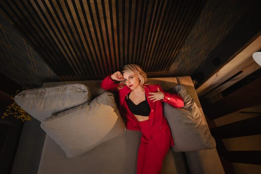 a beautiful girl dressed in a red formal suit posing in a modern interior.