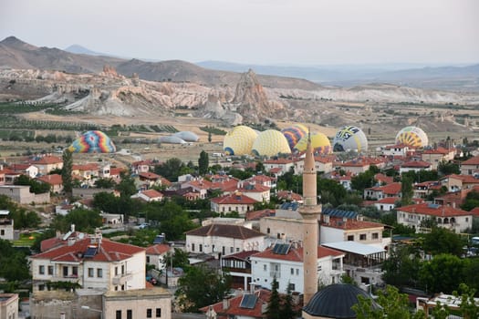 Aerial view of the village of Cavusin, the minaret and hot air balloons in the background in Turkey