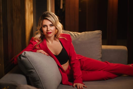 a beautiful girl dressed in a red formal suit posing in a modern interior.