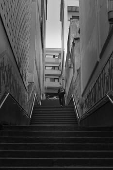 Grayscale shot of a man climbing stairs between buildings