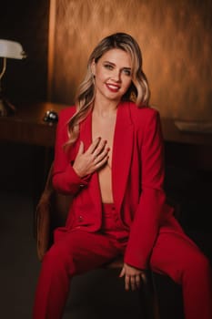 a beautiful girl dressed in a red formal suit posing in a modern interior.