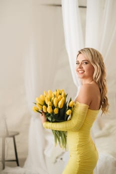 a happy woman in a yellow dress embraces a bouquet of yellow spring tulips in the interior.