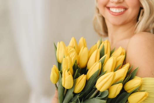 a happy woman in a yellow dress embraces a bouquet of yellow spring tulips in the interior.