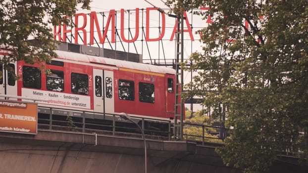 Red train passing on a bridge surrounded with trees in front of Bermudadreieck in Bochum, Germany