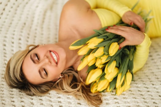 a happy woman in a yellow dress embraces a bouquet of yellow spring tulips in the interior.