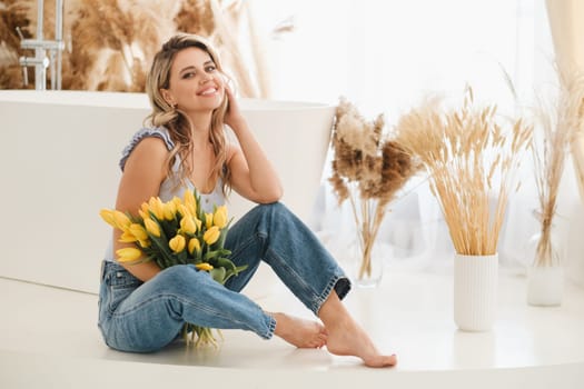 Cute smiling girl with a bouquet of yellow tulips in the interior.