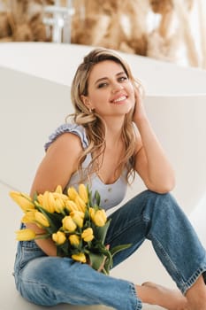 Cute smiling girl with a bouquet of yellow tulips in the interior.