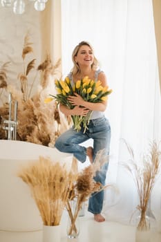 Cute smiling girl with a bouquet of yellow tulips in the interior.