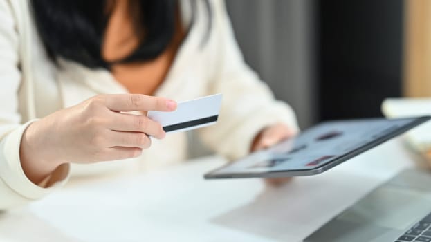 Woman hand holding credit card and using digital tablet, making orders via internet or transaction on bank application.