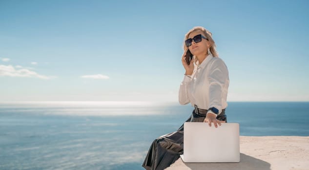 Freelance women sea working on a computer. Pretty middle aged woman with computer and phone outdoors with beautiful sea view. The concept of remote work