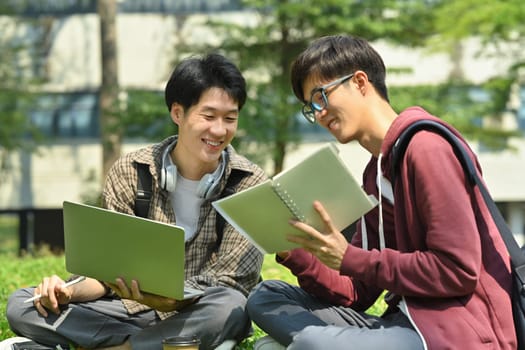 Two asian college student making research, working on group project on laptop at outdoor on green lawn at university.