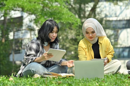 Young Asian college students working on laptop, preparing for an exam at outdoor. Education, technology and community concept.