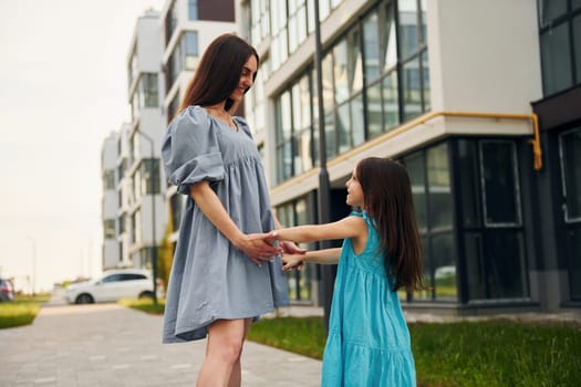 Young mother with her little daughter walking near the buildings.