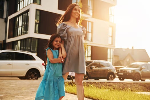 Beautiful sunshine. Young mother with her little daughter walking near the buildings.