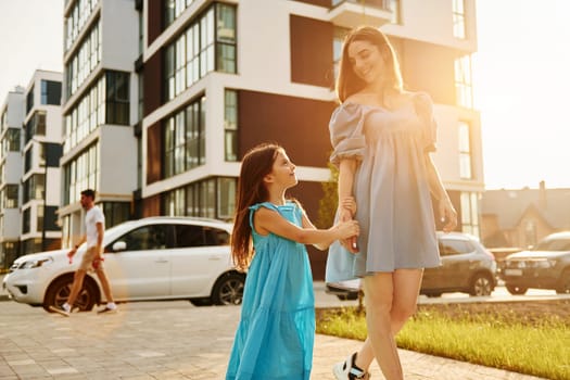 Beautiful sunshine. Young mother with her little daughter walking near the buildings.