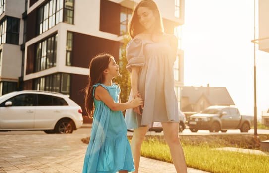 Beautiful sunshine. Young mother with her little daughter walking near the buildings.