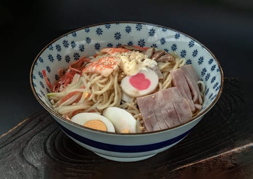 Cold noodles (Ramen) with roast pork sliced, shrimp, ham, boiled egg and lemon sauce in blue ceramic bowl on wooden tray. Japanese style noodles, Healthy life style eating and Asian food concept. Space for text, Selective focus.