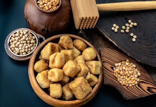 Brown fried tofu puffs or Deep Fried Tofu in wooden bowl and grains (soybeans) with dark background. Space for text.