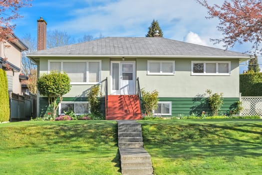 Average residential house on land terrace with concrete stairs over front yard lawn