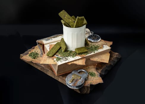 Bangkok, Thailand - Mar 17, 2023 : Homemade Cannabis Snack Sticks in the steel cup are on the Old Song Book with the Analog Pocket Watch and Vintage Iron Padlock on old wooden plank with dark backgroud. The Concept of Relaxation and the Happiness, Vintage style, Space for text.