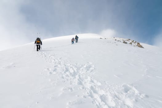 Mountaineers walking up along a snowy ridge with the skis in the backpack. Skier on the climbing track for freeride-descent. Backcountry skiers. ski free rider climbs the slope into deep snow powder.