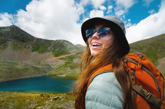 portrait of a girl in the mountains standing looking at the mountain landscape. Traveler portrait. The concept of adventure, travel and hiking. Happy woman in a cap enjoys the sunshine while hiking in the mountains. Tourist with glasses.
