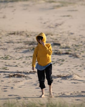 Kid enjoys hiding his face with hood in the beach sand.