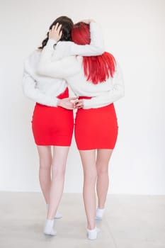 Rear view of two women dressed in identical red dresses and white sweaters. Lesbian intimacy. White background