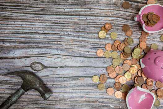 Broken piggy bank smashed into pieces with hammer, with cash and coins on wooden background top view with copy space, money savings concept space for text