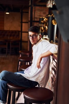 On the chair. Man in casual clothes sitting in the pub.