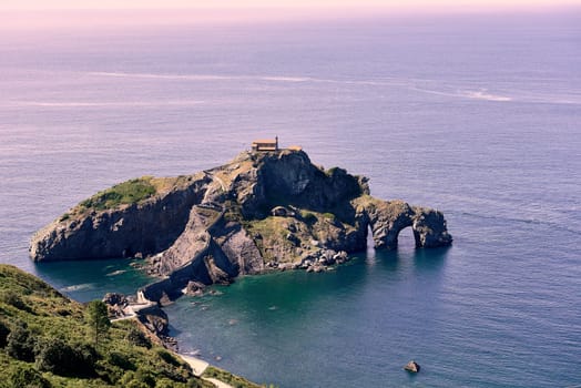 Hermitage of San Juan de Gaztelugatxe on a sunny day. calm sea, rocky formation, holes, frame of branches and trees