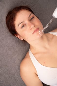 The doctor uses the darsonval apparatus against acne on the face of a female patient