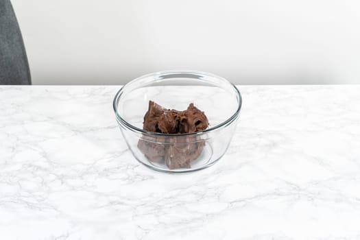 Mixing store-bought chocolate frosting in a mixing glass bowl with a hand mixer.