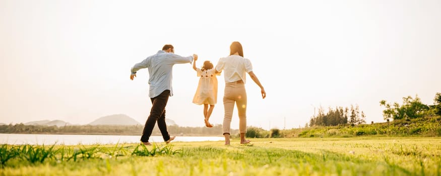 Back view of Happy Asian family walking and playing together in a scenic garden, with a beautiful sunset in the background and a feeling of fun and enjoyment, Family day