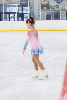 Little girl practicing figure skating on an indoor ice rink.