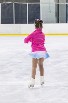 Little girl practicing figure skating on an indoor ice rink.