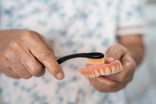 Asian elderly woman patient use toothbrush to clean partial denture of replacement teeth.