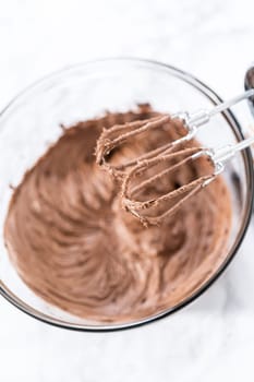 Mixing store-bought chocolate frosting in a mixing glass bowl with a hand mixer.