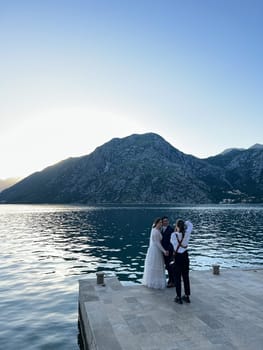 Kotor, Montenegro - 12.07.22: Girl-photographer photographs bride and groom standing on the pier by the sea. High quality photo