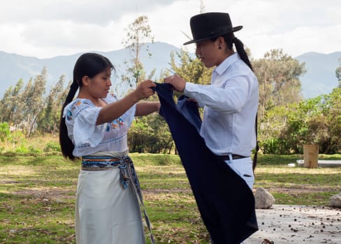 Indigenous man lovingly helps his wife get ready in her traditional dress for a cultural celebration. High quality photo