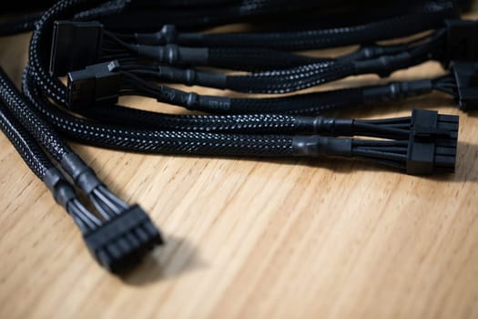 Black modular power cables for a computer lying on a brown wooden top. Close-up of black computer cables. Blurred foreground. A focused view of the cables in the background.