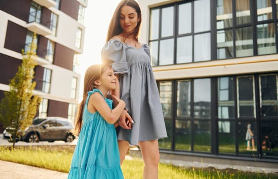 Beautiful sunshine. Young mother with her little daughter walking near the buildings.