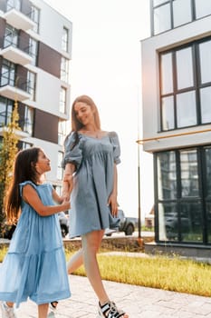 Illuminated by sunlight. Young mother with her little daughter walking near the buildings.