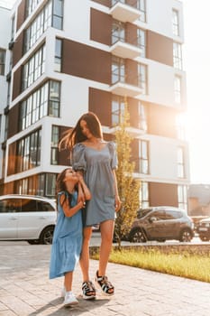 Illuminated by sunlight. Young mother with her little daughter walking near the buildings.