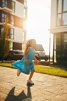 Cheerful little girl walking outdoors in the city in dress.