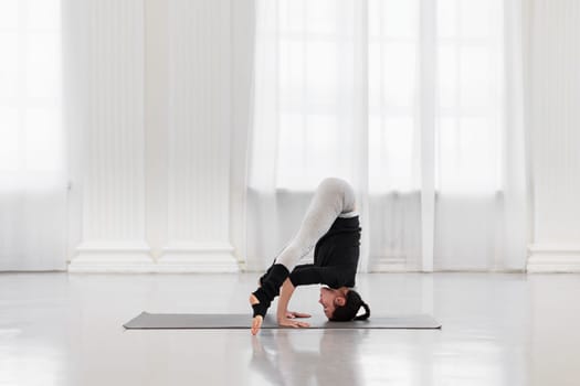 Slim young woman doing headstand preparation during yoga class in bright gym. Concept of relieving tension in the body, relaxation, improving metabolism, balance and concentration.