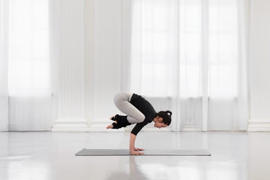 Side view of charming woman doing bakasana during yoga meditation in a bright gym. The concept of arm strength and endurance, flexibility and balance.