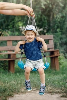 Mother swing her son. Little boy very happy on a swing outdoor.